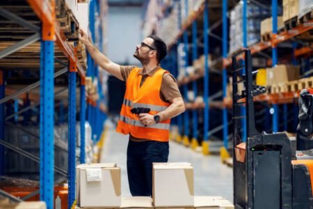 A supervisor with scanner in hands checking on goods in boxes in storage.