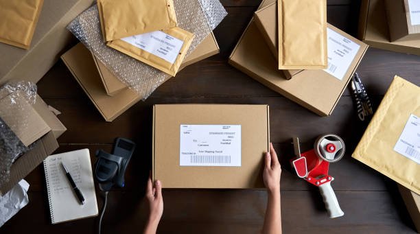 Above table top view of female warehouse worker or seller packing e-commerce shipping order box for dispatching.