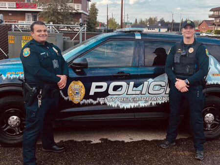 Two policemen from Alaska Fairbanks department are standing in front of a police car.