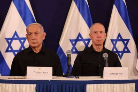 Netanyahu and Gallant sitting together in front of Israeli flags.