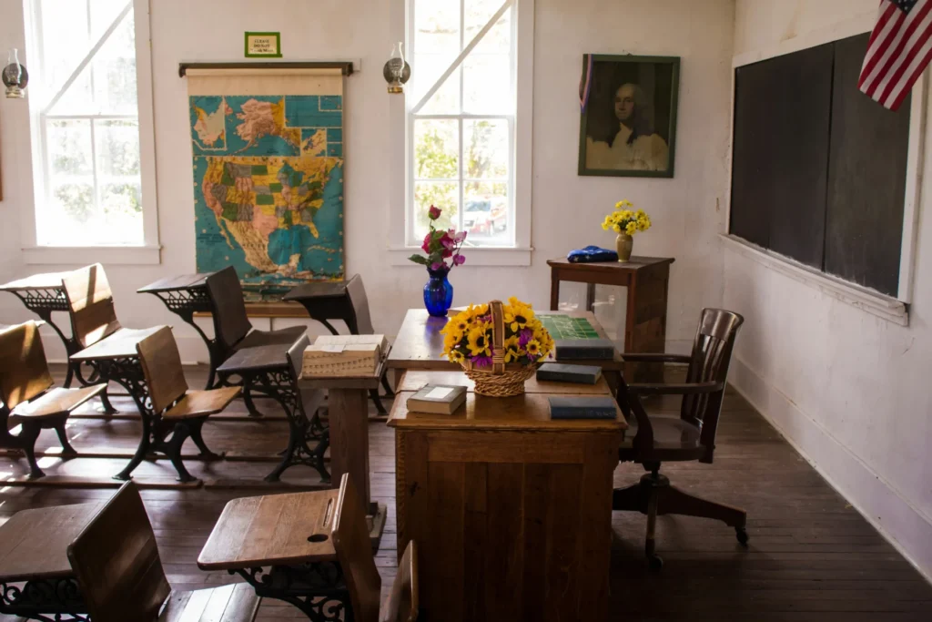 A classroom with tables and chairs and black chalk board.