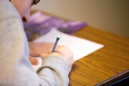 Alaska’s Academic Performance Falls Short Across State A student is writing on a paper with a pencil.