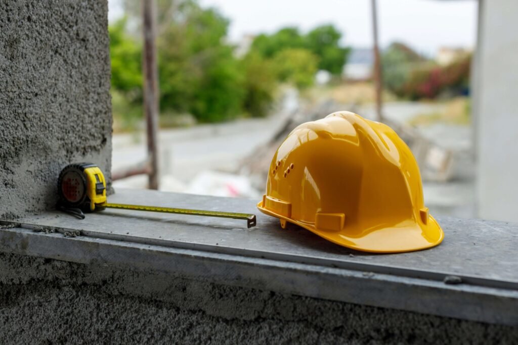 A yellow hard hat and a measuring tape sitting on top of a cement wall.