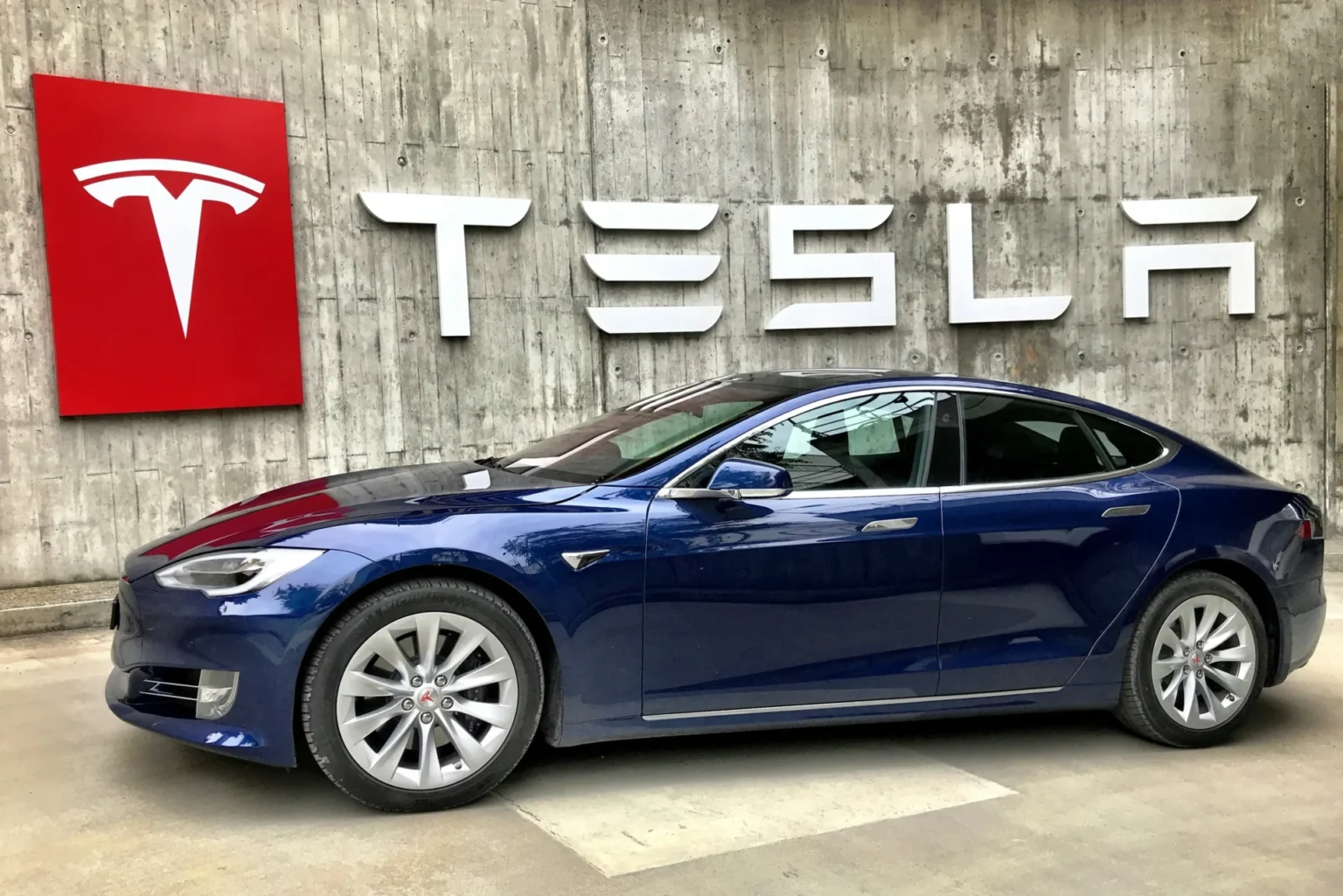 Tesla’s EV Sales Decline In 2024 Amid Stiff Competition A Tesla parked in front of a wall with a Tesla logo on it.