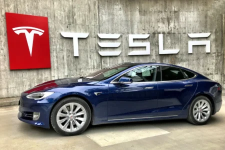 A Tesla parked in front of a wall with a Tesla logo on it.