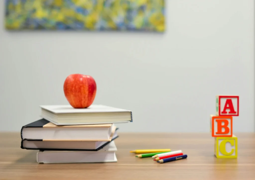 A table with a stack of books, building blocks, and an apple.