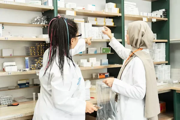 two female pharmacist standing in front of medicine shelf
