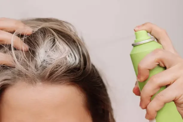 Beyond The Basics: How To Use Dry Shampoo To Extend Your Hair Care Routine a girl using dry shampoo in her hairs